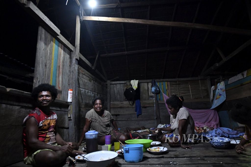 Warga menikmati makan malam bersama dengan penerangan lampu yang menggunakan sumber listrik dari tabung listrik di Kampung Munggui, Distrik Windesi, Kabupaten Kepulauan Yapen, Papua, Rabu (29/9/2021). Sebelum menikmati listrik menggunakan alat penyimpanan daya listrik atau tabung listrik, warga menggunakan pelita sebagai sumber penerangan saat malam hari.  