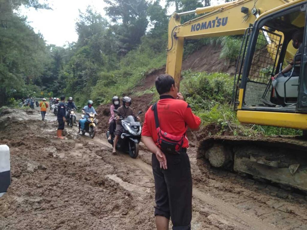 Pengendara motor satu per satu melewati alat berat yang digunakan untuk menyingkirkan material longsor di area Hutan Gledug, Sempor, Kebumen, Jawa Tengah, Kamis (1/7/2021). Tidak ada korban jiwa dalam longsor ini.