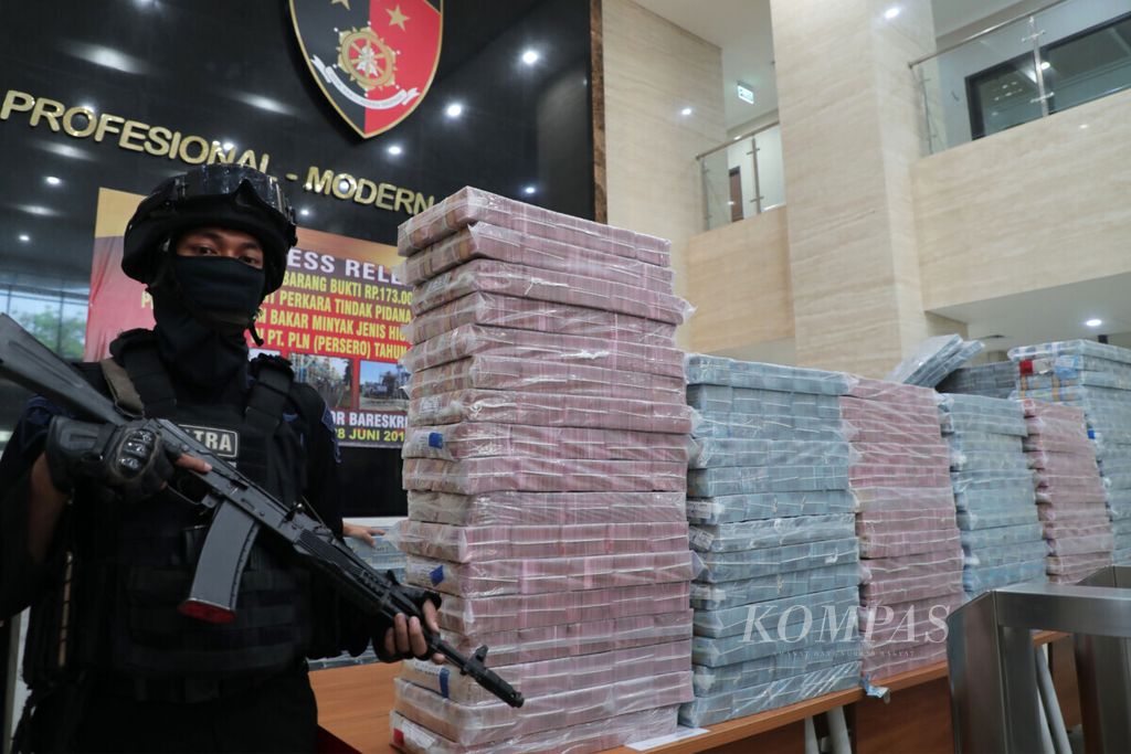 Polisi berjaga di samping uang yang dijadikan barang bukti saat pengungkapan tindak pidana korupsi dalam pengadaan BBM jenis <i>high speed </i>Diesel PT PLN Tahun Anggaran 2010 di Gedung Bareskrim, Mabes Polri, Jakarta, Jumat (28/6/2019). 