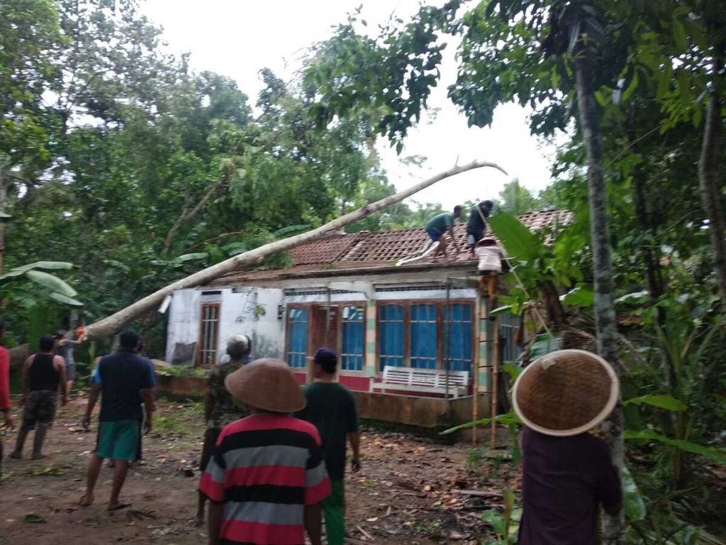 Warga bergotong-royong membersihkan puing rumah yang rusak tertimpa pohon tumbang di Sidareja, Kabupaten Cilacap, Jawa Tengah, Kamis (12/12/2019) sore. Potensi angin kencang diprediksi masih terjadi hingga awal Januari 2020. Masyarakat diimbau waspada.