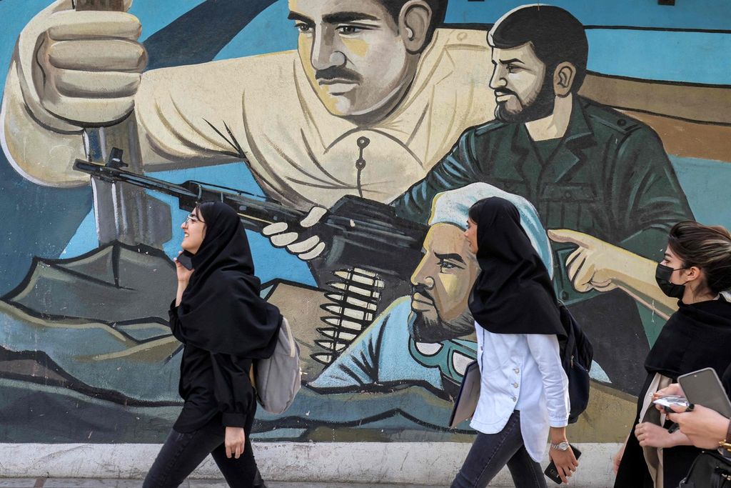 Sejumlah perempuan berjalan melintas di depan tembok dengan mural bertema anti-Israel di dekat Alun-Alun Palestina di Teheran pada Minggu (14/4/2024).