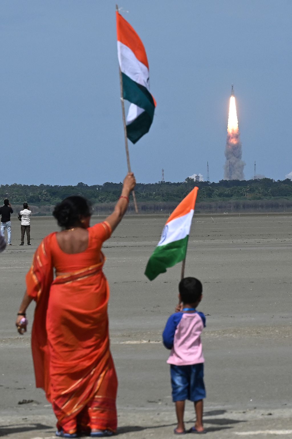 Seorang ibu dan anak mengibarkan bendera India saat roket pengangkut wahana Chandrayaan-3 meluncur dari Pusat Antariksa Satish Dhawan di Sriharikota, pulau di lepas pantai Negara Bagian Andhra Pradesh, India, Jumat (14/7/2023). 