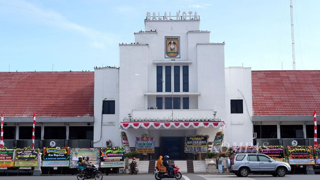 Warga melintas di depan Balai Kota Banjarbaru, Kalimantan Selatan, yang penuh dengan karangan bunga, Selasa (11/8/2020). Sehari sebelumnya, Wali Kota Banjarbaru Nadjmi Adhani meninggal dunia di Banjarmasin akibat menderita Covid-19.
