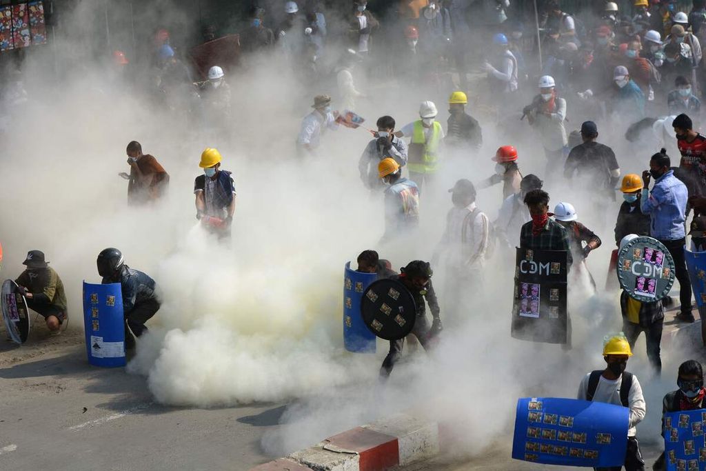 Dalam foto yang diambil pada 2 Maret 2021 ini tampak para pengunjuk rasa bertahan ketika aparat menembakkan gas air mata ke arah mereka. Unjuk rasa itu digelar di Kale, Myanmar.