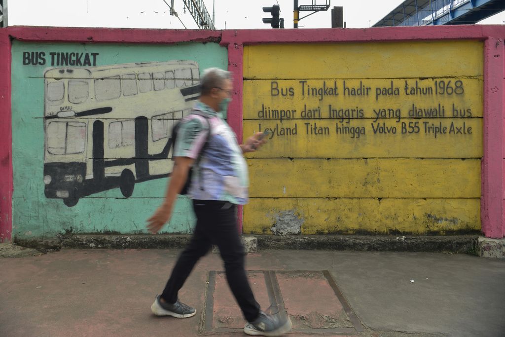 Seorang warga melintas di samping mural yang telah kusam di tembok pembatas sekitar Stasiun Jatinegara, Jakarta Timur, Rabu (18/1/2023). 