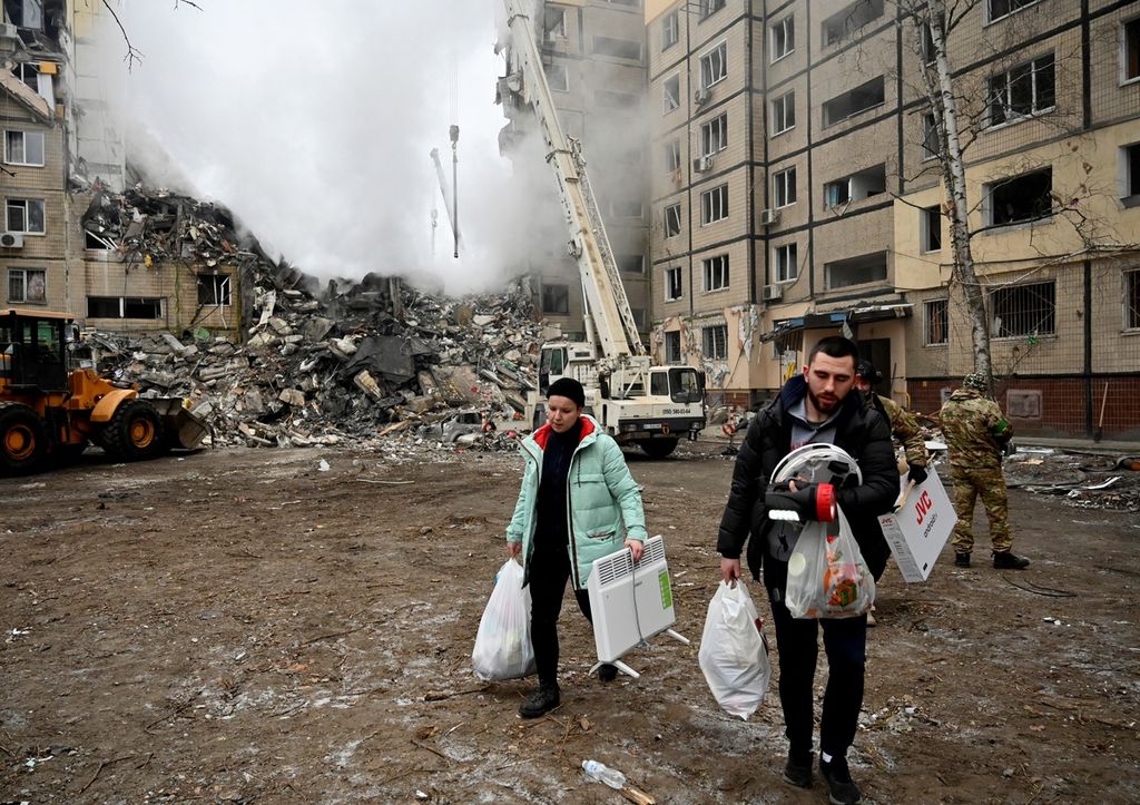 Warga membawa barang-barang mereka dari bangunan tempat tinggal yang hancur setelah serangan rudal di Dnipro, Ukraina, Minggu (15/1/2023).