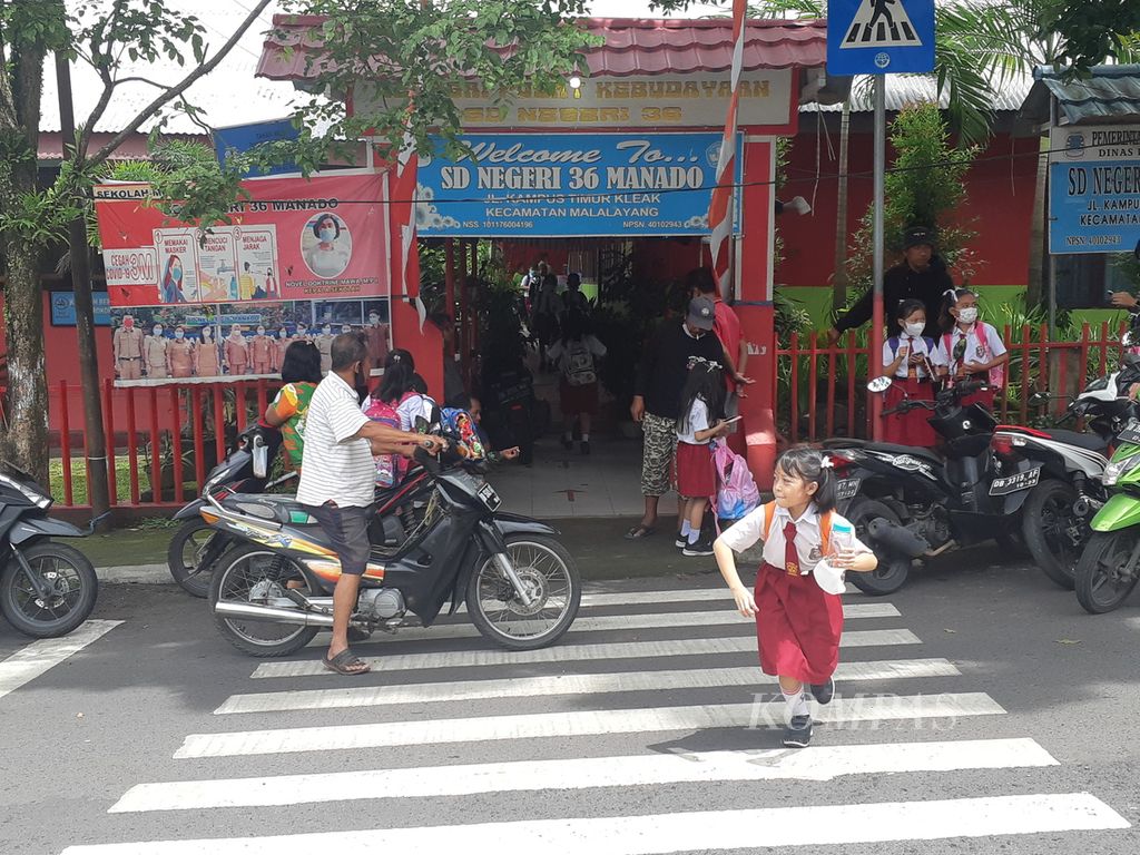 Seorang siswi SD Negeri 36 Manado di bilangan Kleak, Manado, Sulawesi Utara, menyeberangi jalan sepulang sekolah, Selasa (8/2/2022). Pembelajaran tatap muka telah diberlakukan penuh di Sulut seiring dengan berlangsungnya program vaksinasi bagi anak berusia 6-11 tahun dan 12-17 tahun.