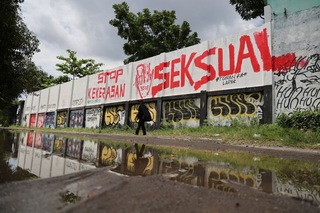 Warga melintas di depan mural berisi seruan untuk mendorong pengesahan Rancangan Undang-Undang Tindak Pidana Kekerasan Seksual yang dibuat di tembok Stadion Kridosono, Yogyakarta, Senin (10/1/2021). 