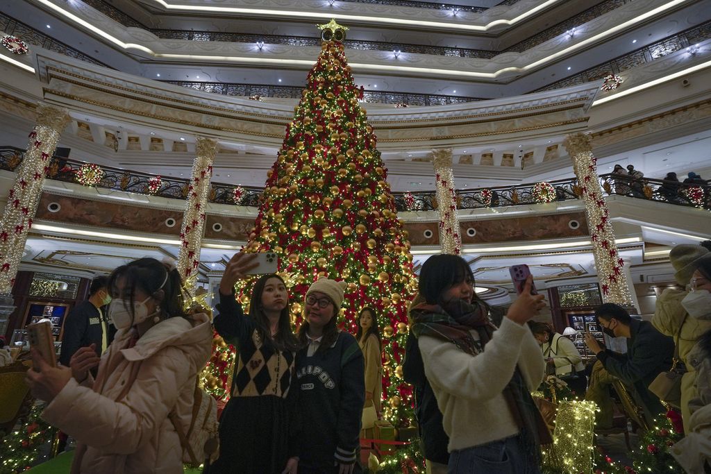 Sejumlah warga berswafoto dengan latar belakang pohon natal di sebuah pusat perbelanjaan di Beijing, China, Sabtu (24/12/2022). Di tengah melonjaknya kasus harian Covid-19 di China, Komisi Kesehatan Nasional China menghentikan publikasi data kasus harian dan kematian akibat Covid-19. 