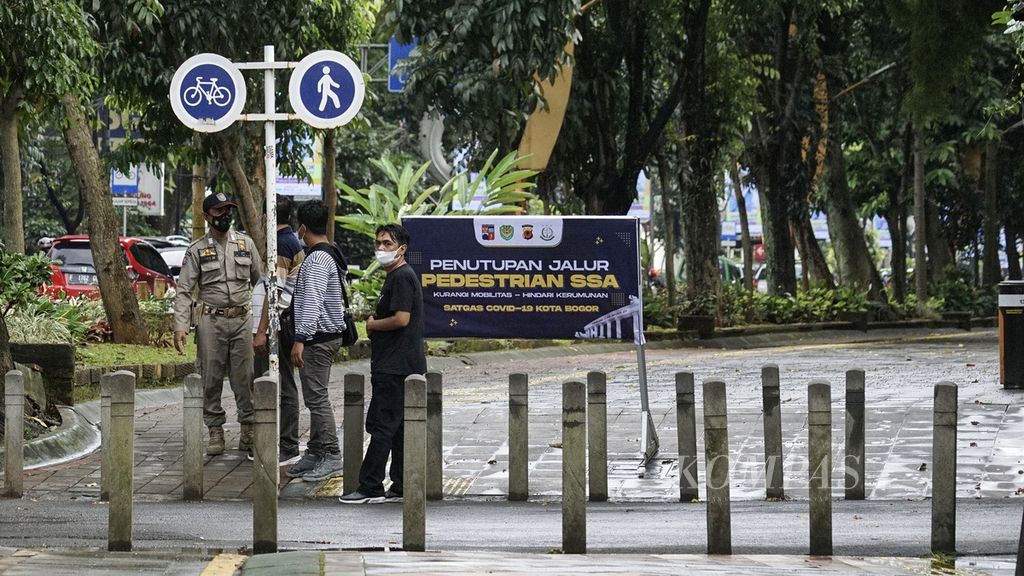 Petugas Satuan Polisi Pamong Praja menghimbau warga di Jalur pedestrian di kawasan sistem satu arah (SSA) Kota Bogor, Jawa Barat, yang ditutup bagi aktivitas umum, Minggu (6/2/2022). 