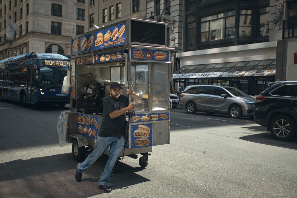 Seorang pria menarik gerobak tempat ia berjualan <i>hotdog</i> di Fifth Avenue, New York City, AS, Rabu (27/7/2022). 