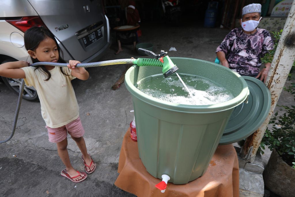 Seorang anak membantu mengisi ember penampungan air untuk cuci tangan di depan rumah salah satu warga di RW 014 Grogol Utara, Kebayoran Lama, Jakarta Selatan, Minggu (5/7/2020).