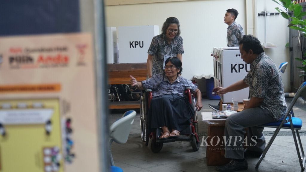 Esti (60), seorang penyandang disabilitas, dibantu petugas TPS mencelupkan jarinya ke tinta seusai memberikan suara di TPS 114, Kelurahan Cilandak, Kecamatan Cilandak Barat, Jakarta, pada Pemilu 2019, Rabu (17/4/2019). Ia merasa kesulitan dalam mencoblos karena meja yang digunakan lebih tinggi daripada tubuhnya. 