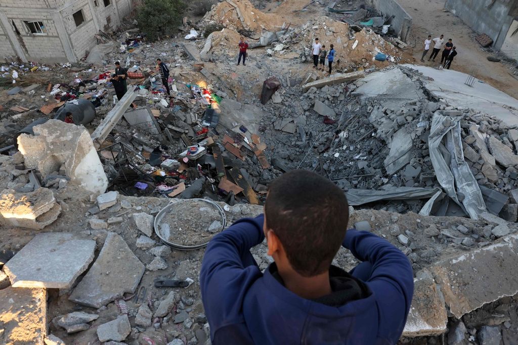  Seorang anak muda memandang orang-orang yang sedang memeriksa reruntuhan bangunan yang dibom Israel di Rafah, Jalur Gaza, pada 21 Oktober 2023.