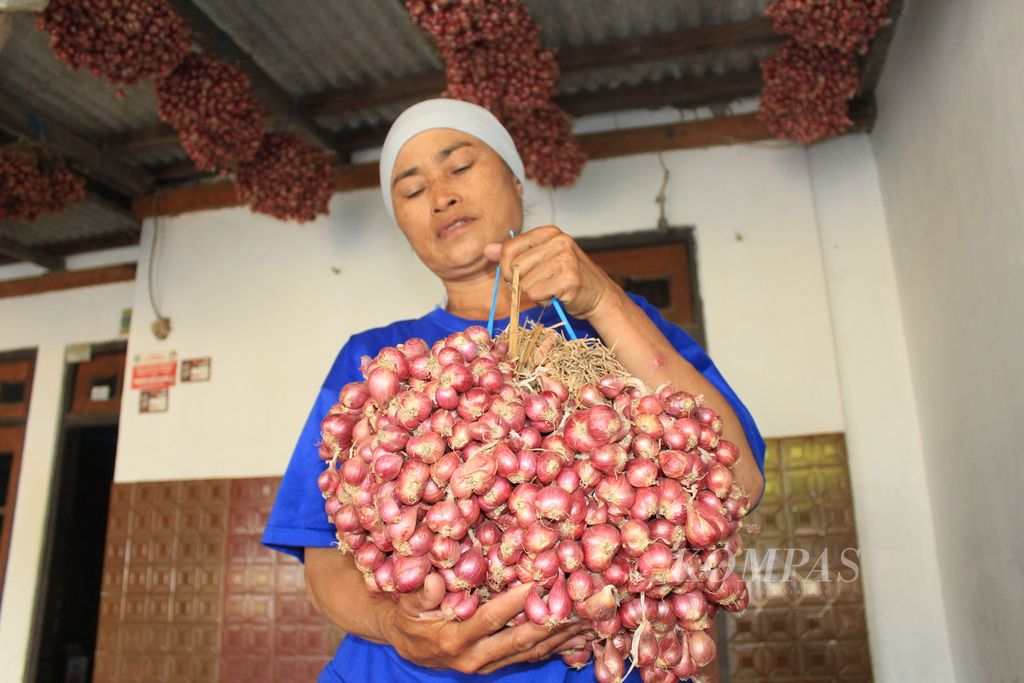 Surmi (51), perempuan buruh tani, menunjukkan hasil panen bawang merah yang digantung di rumahnya di Desa Mekarsari, Kecamatan Patrol, Kabupaten Indramayu, Jawa Barat, Kamis (12/10/2023) siang. Bawang itu berasal dari lahan garapannya di sekitar Pembangkit Listrik Tenaga Uap Indramayu 2.