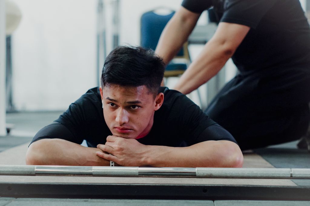 Lifter Indonesia, Rizki Juniansyah, dipijat sebelum memulai latihan persiapan Olimpiade Paris 2024 di Mess Kwini, Jakarta, Jumat (24/5/2024). Rizki didampingi seorang pemijat. Dia biasanya dipijat setiap sebelum dan sehabis latihan.