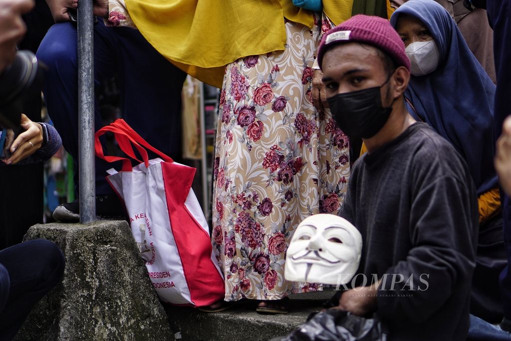 Ijun (21) menunjukkan topeng Guy Fawkes yang ia buat sendiri di antara kerumunan warga yang melihat kunjungan Presiden Joko Widodo ke Pasar Sepinggan, Kota Balikpapan, Kalimantan Timur, Senin (31/1/2022).