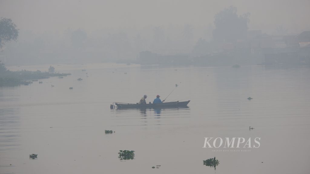 Warga mencari ikan di Sungai Martapura yang diliputi kabut asap di Kota Banjarmasin, Kalimantan Selatan, Selasa (3/10/2023) pagi.