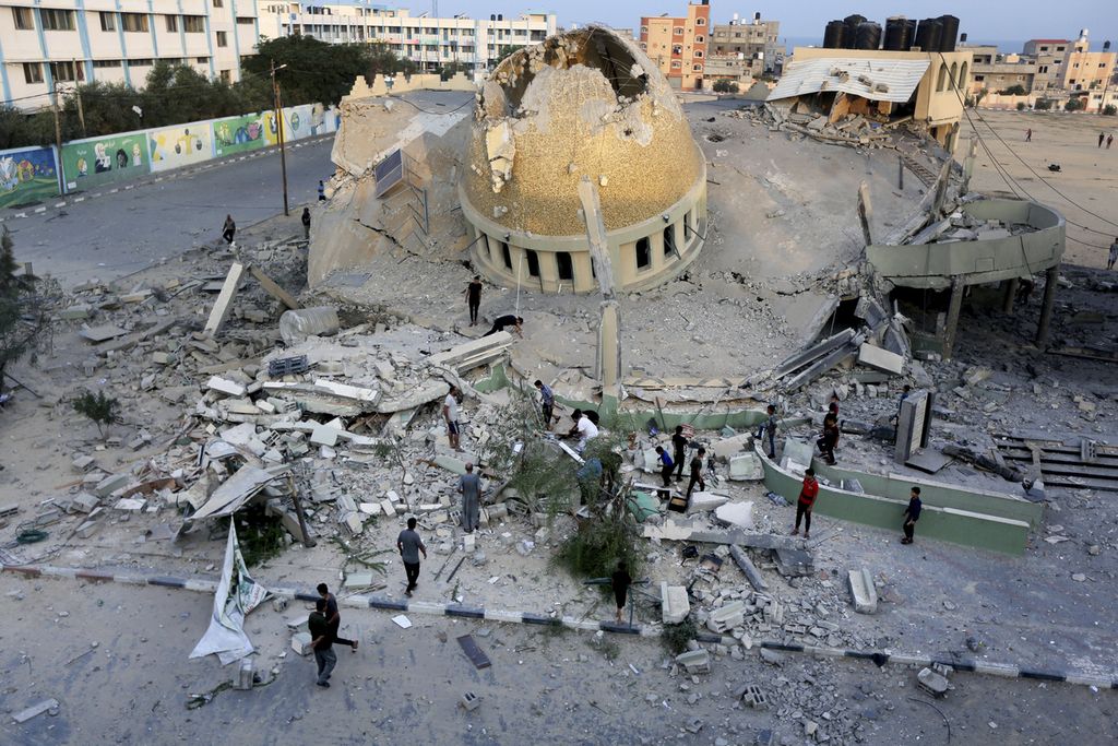 Orang-orang berdiri di luar masjid yang hancur akibat serangan udara Israel di Khan Younis, Jalur Gaza, Minggu (8/10/2023). 