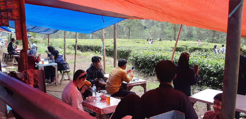 Wisatawan menikmati makanan dan minuman yang dijajakan di pinggir jalan sambil memandang ke perkebunan teh di kawasan Gunung Mas, Cisarua, Kabupaten Bogor, Jawa Barat, Kamis (3/3/2022).