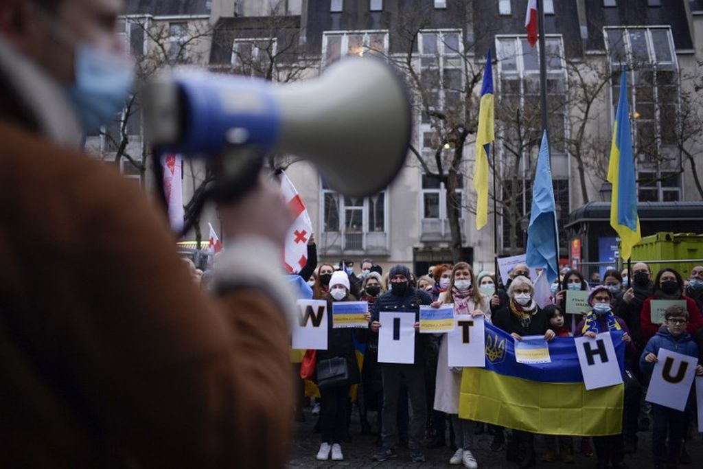 Protestors hold signs and Ukranian flags during a demonstration in Paris, on January 29, 2022 in support with Ukraine as Russian troops gathered at the Ukrainian-Russian border. - The Kremlin has deployed over 100,000 troops and heavy armour along Ukraine's borders, according to the West, which fears that the Kremlin will stage an incursion.