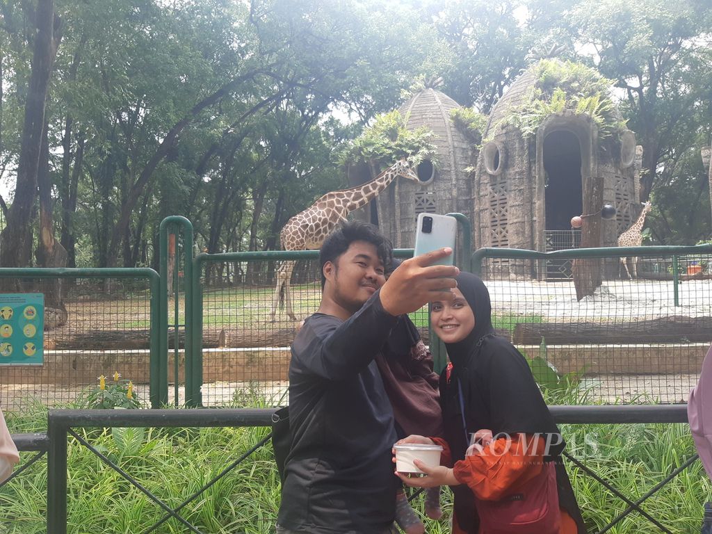 Pengunjung berfoto denga latar belakang penangkaran jerapah di Taman Margasatwa Ragunan, Jakarta Selatan, Senin (25/12/2022). Jumlah pengunjung tempat wisata itu mencapai 93.000 pada libur akhir pekan, Minggu (24/12/2023).