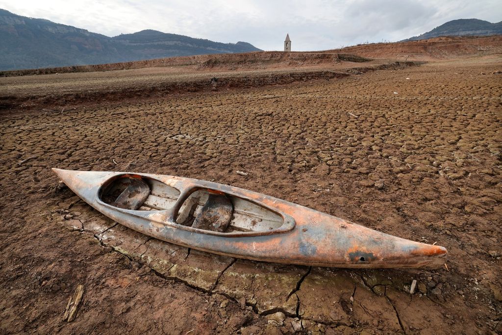 A kayak is stranded on dry land next to the low water level of Lake Sau, with the background of the Sant Roma de Sau Church, in the province of Girona in Catalonia, on Monday (15/1/2024). The Catalonia region in the northeast of Spain declared a drought emergency on February 1, 2024, for Barcelona and its surrounding areas.