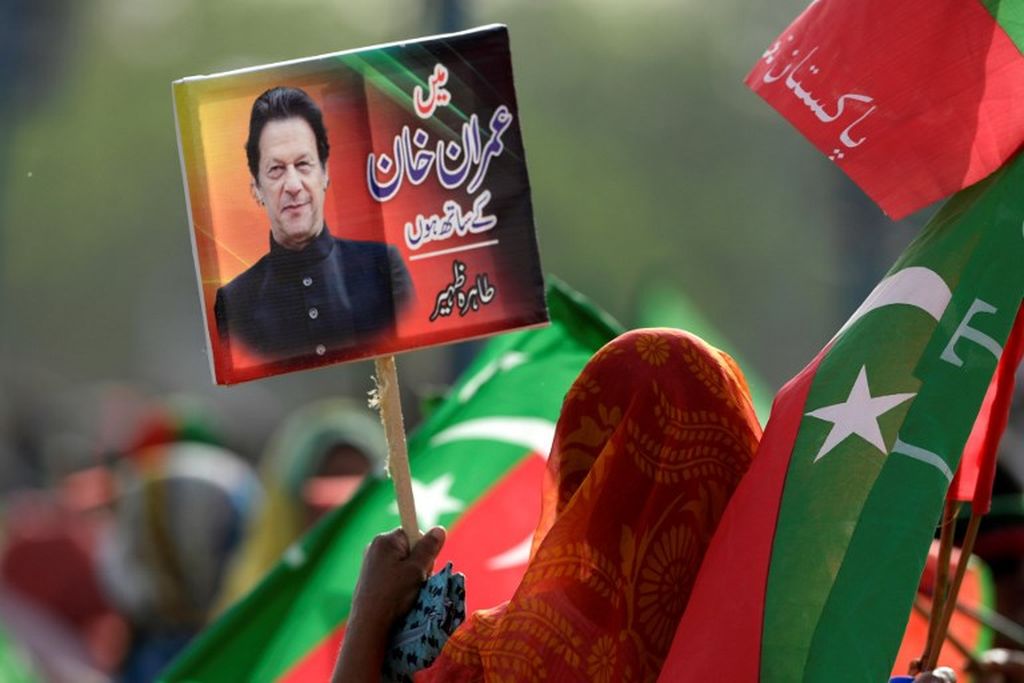 Seorang pendukung atau suporter partai berkuasa, Pakistan Tehreek-e-Insaf (PTI), mengangkat plakat fofo Perdana Menteri Pakistan Imran Khan selama pawai di Islamabad, 27 Maret  2022. 