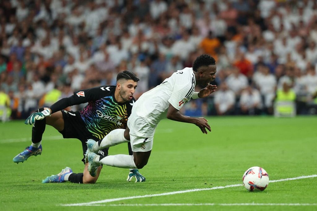 Pemain Real Madrid, Vinicius Junior (kanan), dijatuhkan kiper Real Betis, Rui Silva, pada laga Liga Spanyol di Stadion Santiago Bernabeu, Madrid, Minggu (1/9/2024). 