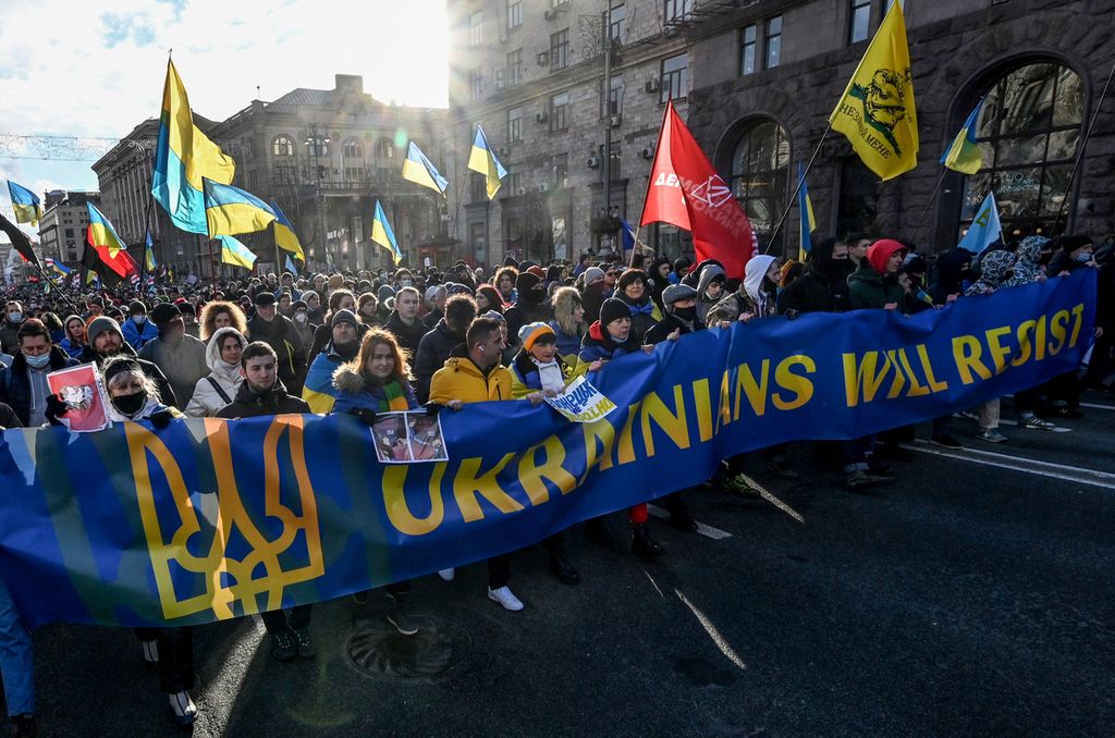Para demonstran meneriakkan slogan-slogan saat mereka berbaris di belakang spanduk sambil mengibarkan bendera nasional dalam rapat umum di Kiev, 12 Februari 2022, untuk menunjukkan persatuan di bawah tekanan Rusia.