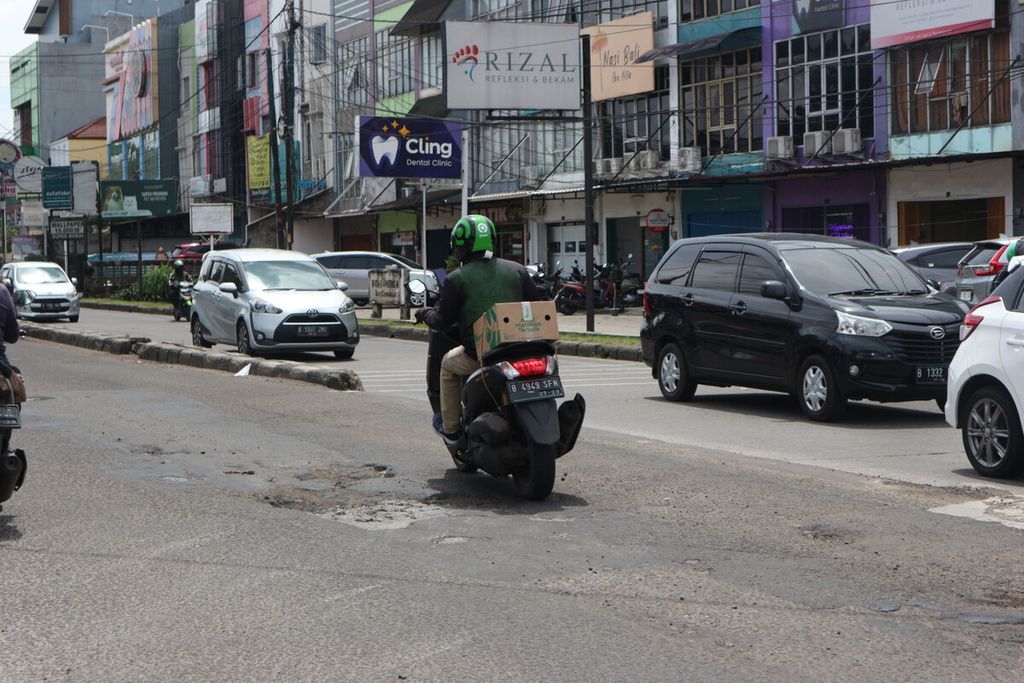Pengendara yang melintas di Jalan Cinere Raya, Depok, menghindari lubang di jalan tersebut, Senin (16/1/2023) siang.