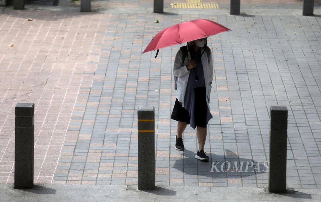 Warga menggunakan payung saat berjalan di kawasan Karet, Jakarta Selatan, Selasa (25/4/2023). Sinar ultraviolet kategori ekstrem hari ini melanda sebagian besar wilayah Indonesia, terutama di kawasan timur dan tengah. 