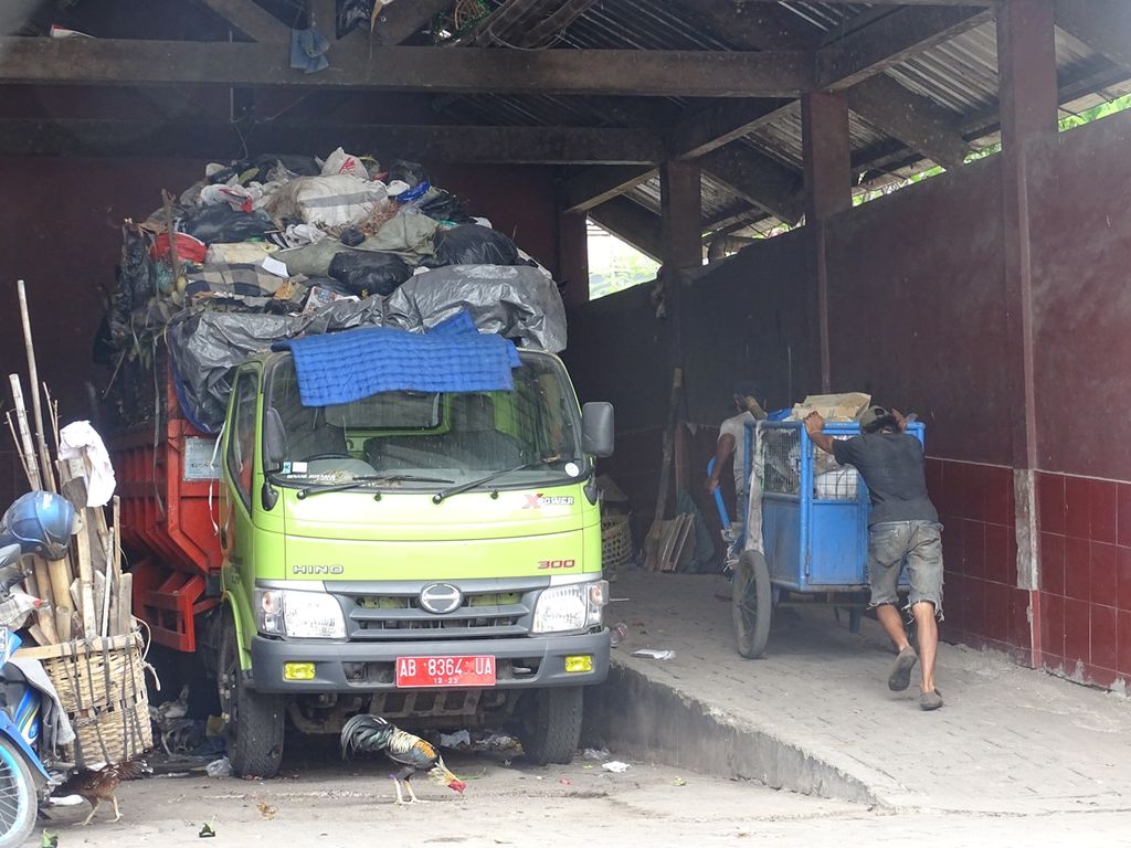 A driver from the Yogyakarta City Environment Agency is helping a garbage collector push a cart filled with trash to a car, at the Garbage Depot, Gedong Kiwo. The waste is then transported into trucks to be disposed of at the final waste disposal site or an integrated waste disposal site in Piyungan, Bantul, Yogyakarta.