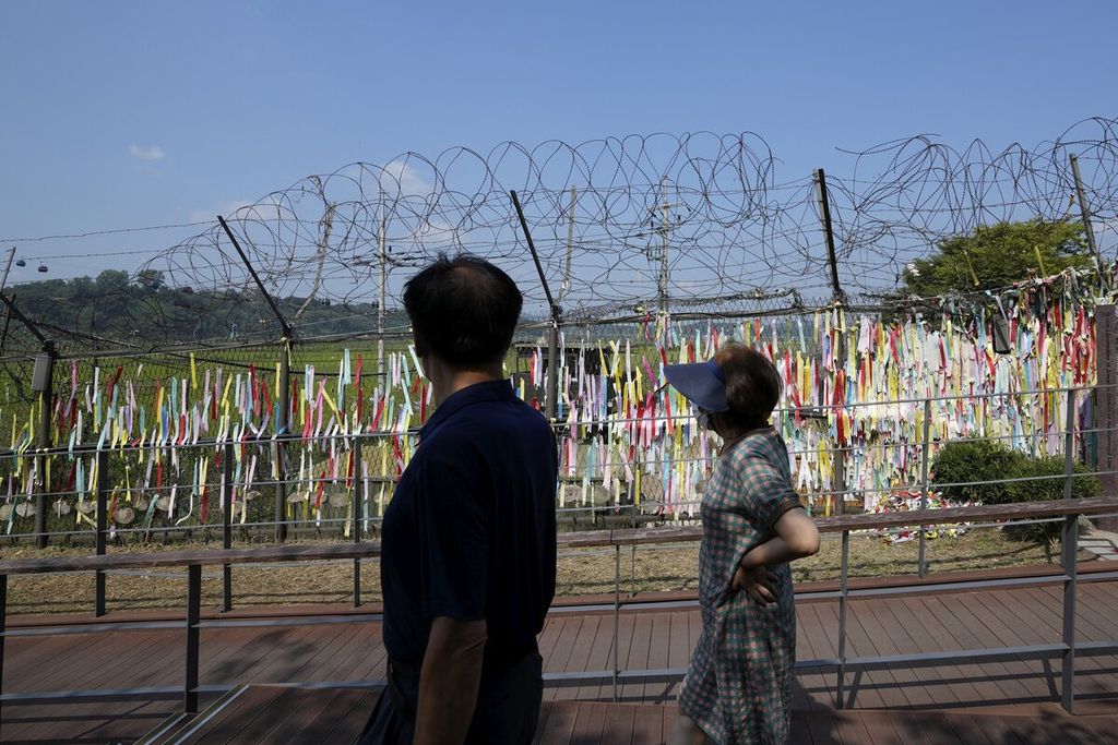 Pengunjung mengenakan masker untuk mencegah penularan Covid-19 berjalan di dekat pagar kawat berduri yang dihiasi pita bertuliskan pesan harapan penyatuan kembali kedua Korea di Paviliun Imjingak di Paju, Korea Selatan, Kamis (9/9/2021).  (AP Photo/Lee Jin-man)