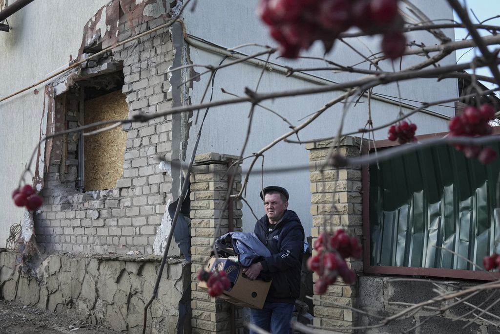 Seorang warga Ukraina tengah membawa sejumlah barang keluar dari rumahnya setelah rumah itu rusak karena terkena serangan artileri yang menyasar Novoluhanske, kota di wilayah Ukraina timur, Rabu (23/2/2022).