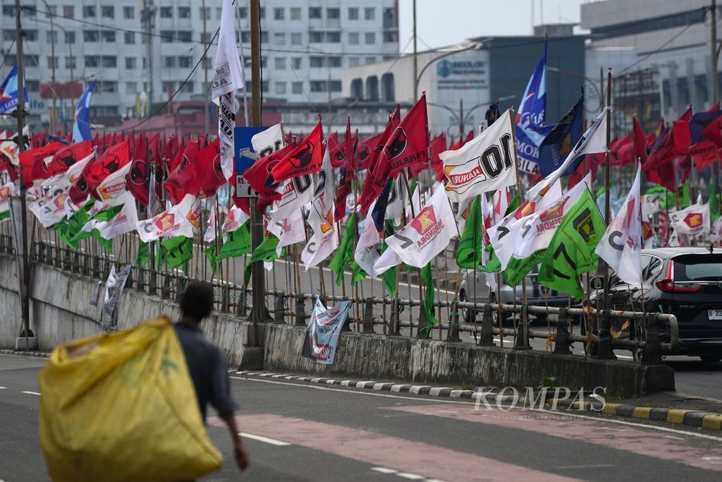 Pemulung melintas di sekitar bendera partai politik peserta Pemilu 2024 yang dipasang di Jalan Pramuka, Jakarta Timur, Senin (1/1/2024). 
