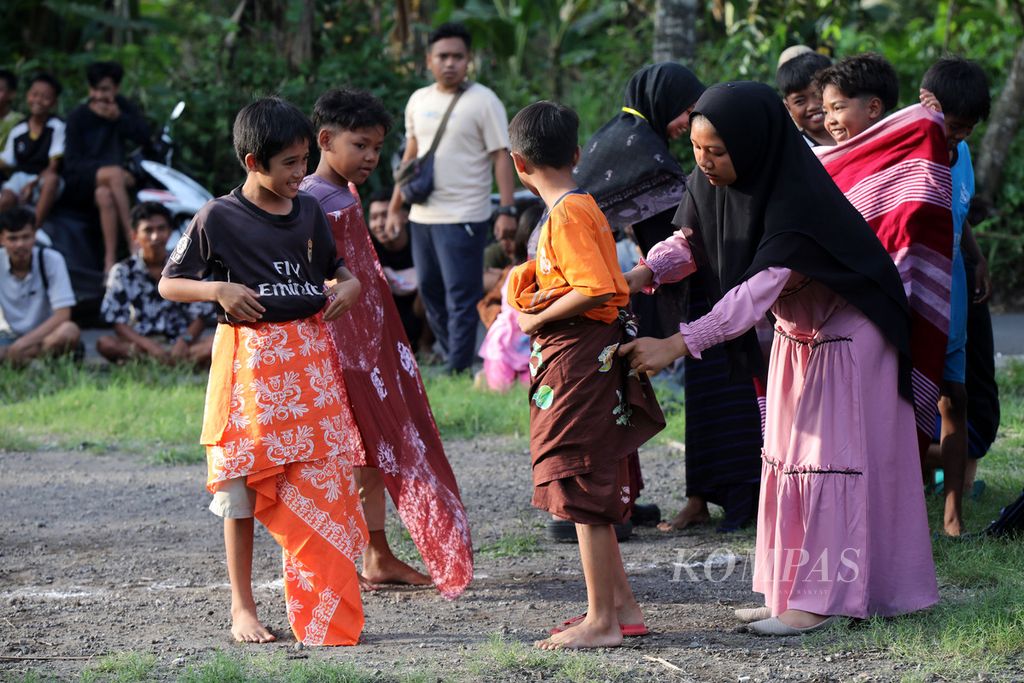 Panitia membantu anak-anak mengenakan kain batik dan tenun sebelum mengikuti lomba permainan tradisional selodor di Desa Pringgasela Selatan, Kecamatan Pringgasela, Lombok Timur, Nusa Tenggara Barat, Minggu (17/12/2023).