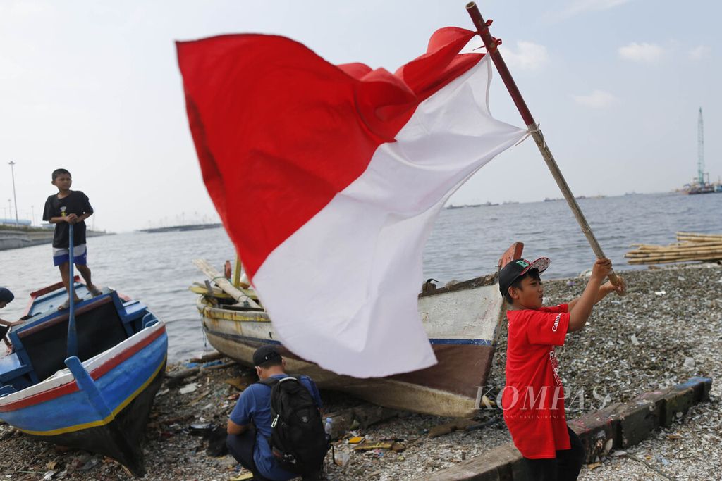 Seorang anak dari komunitas Kelas Jurnalis Cilik mengibar-ngibarkan bendera Merah Putih seusai melaksanakan upacara bendera HUT ke-77 RI di pesisir Kali Baru, Cilincing, Jakarta, Rabu (17/8/2022). Upacara yang dilakukan secara sederhana ini untuk menanamkan benih-benih cinta terhadap Tanah Air sejak dini.