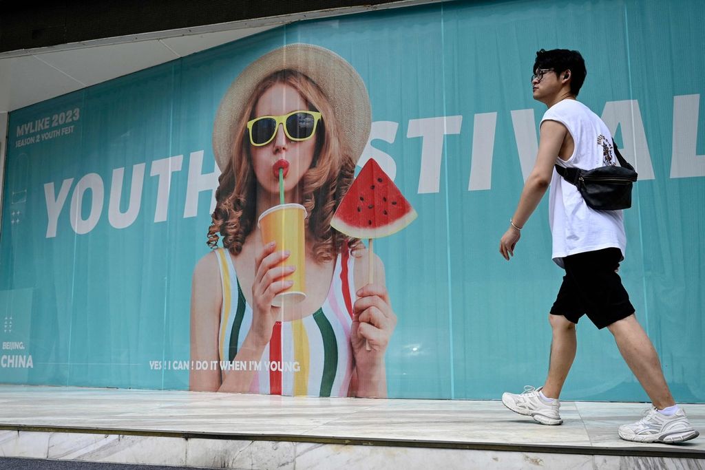 Seorang pemuda berjalan melintas di sebuah sebuah papan iklan di Beijing pada 24 Juli 2023 lalu.