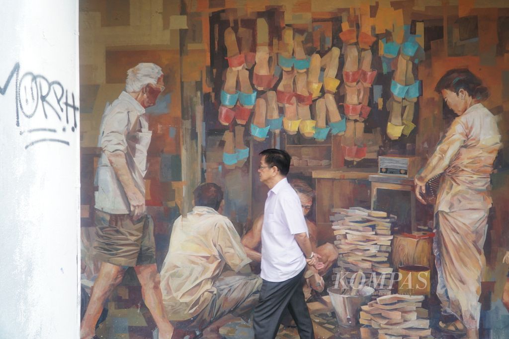 Seorang pria melintas di depan mural yang menggambarkan pembuatan dan jual-beli bakiak di Jalan Ewe Hai, kawasan Kuching Old Bazaar, kota Kuching, Sarawak, Malaysia, Kamis (22/2/2024). 