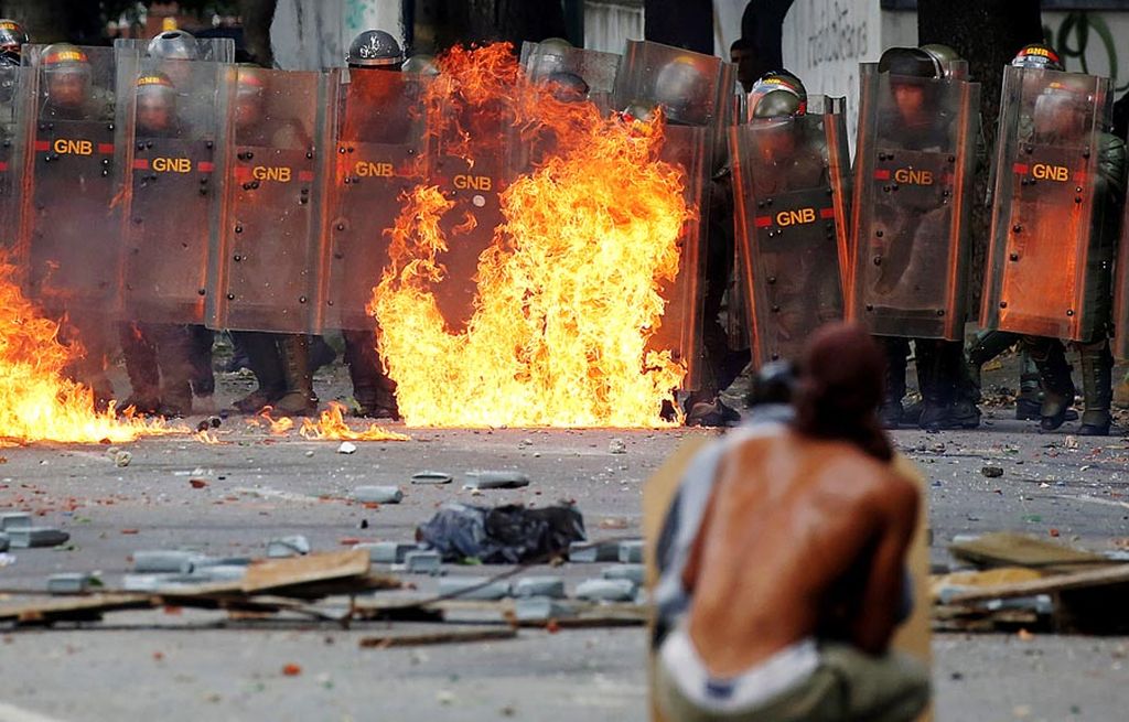   Polisi antihuru-hara  berjaga di belakang api dari bom molotov yang dilemparkan pengunjuk rasa saat terjadi bentrokan dengan para demonstran yang menentang Presiden Nicolas Maduro di Caracas, Venezuela, Rabu (26/7). 