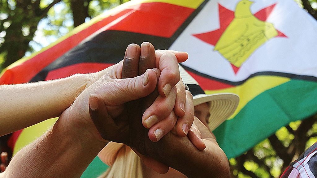 Warga bergandengan tangan  saat menghadiri doa yang digelar di luar Gedung Parlemen di Harare, Zimbabwe, Senin (20/11), untuk mendesak  Presiden  Zimbabwe Robert Mugabe mundur dari jabatannya. 