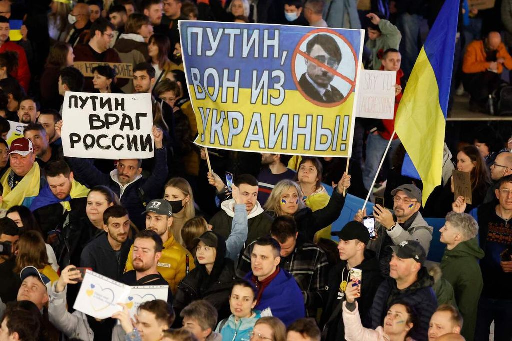 Demonstators hold up a sign showing the Ukrainian flag with text reading in Russian "Putin leave Ukraine" while depicting the Russian president's face as Nazi Germany's Adolf Hitler during a protest against Russia's military operation in Ukraine, in front of the Russian embassy in the Israeli coastal city of Tel Aviv, on February 26, 2022. - In the early hours of February 24, Russia launched an invasion of Ukraine, defying Western outrage and global appeals not to launch a war. 