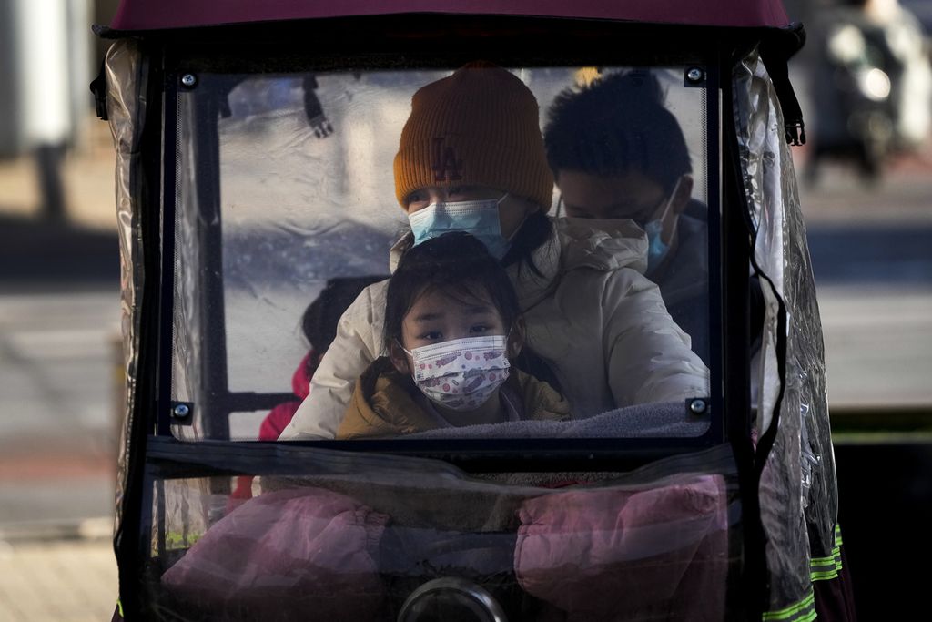 Sebuah keluarga menggunakan masker berkendara dengan kendaraan roda tiga di Beijing, Minggu (18/12/2022). Pelonggaran protokol kesehatan telah membuat jumlah kasus penularan Covid-19 meningkat. 