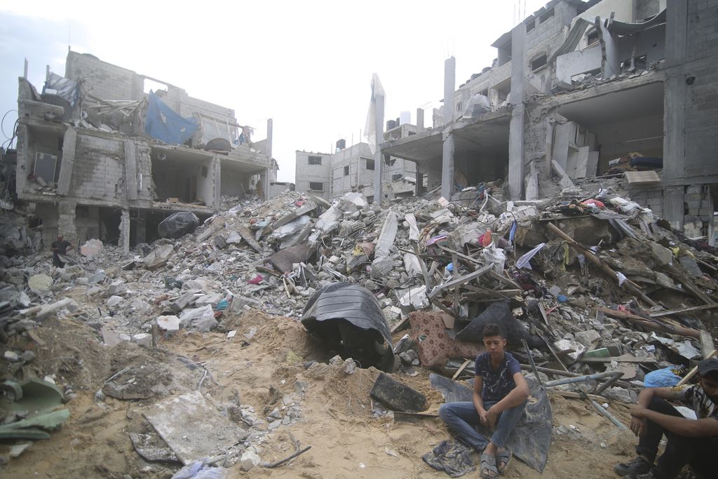 Warga Palestina duduk di dekat reruntuhan bangunan keluarga Abu Helal di kamp pengungsi Rafah, Jalur Gaza, Senin (9/10/2023). 