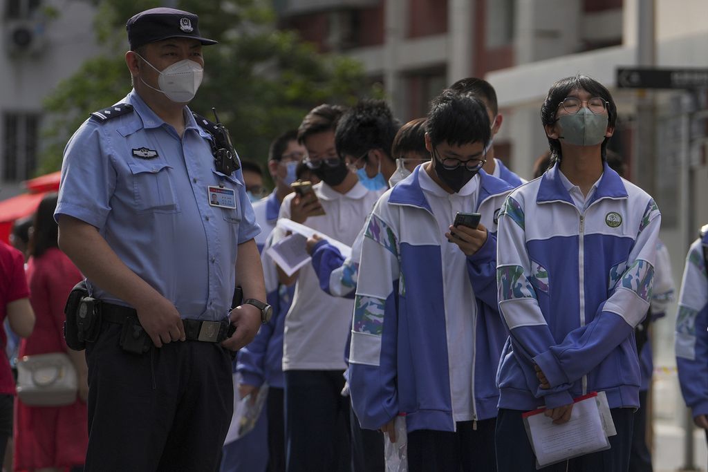 Seorang polisi mengawasi para siswa berbaris memasuki sekolah untuk hari pertama ujian masuk perguruan tinggi nasional China, yang dikenal sebagai gaokao, di Beijing, Selasa, 7 Juni 2022.
