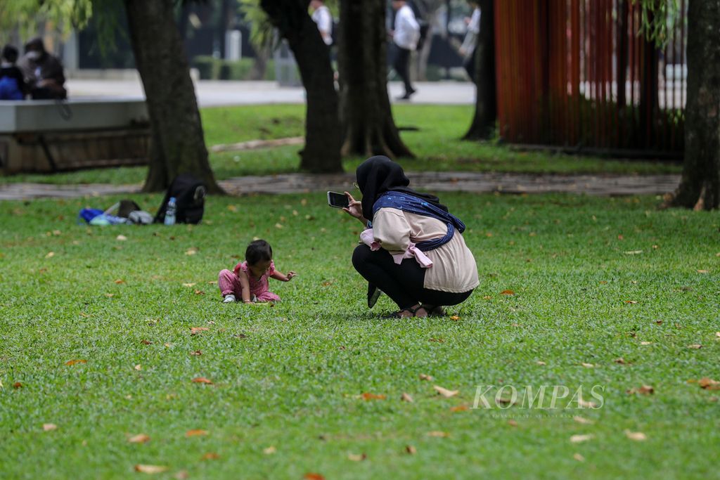 Seorang ibu merekam tingkah laku anaknya saat bermain di Taman Lapangan Banteng, Jakarta, Minggu (2/7/2023).
