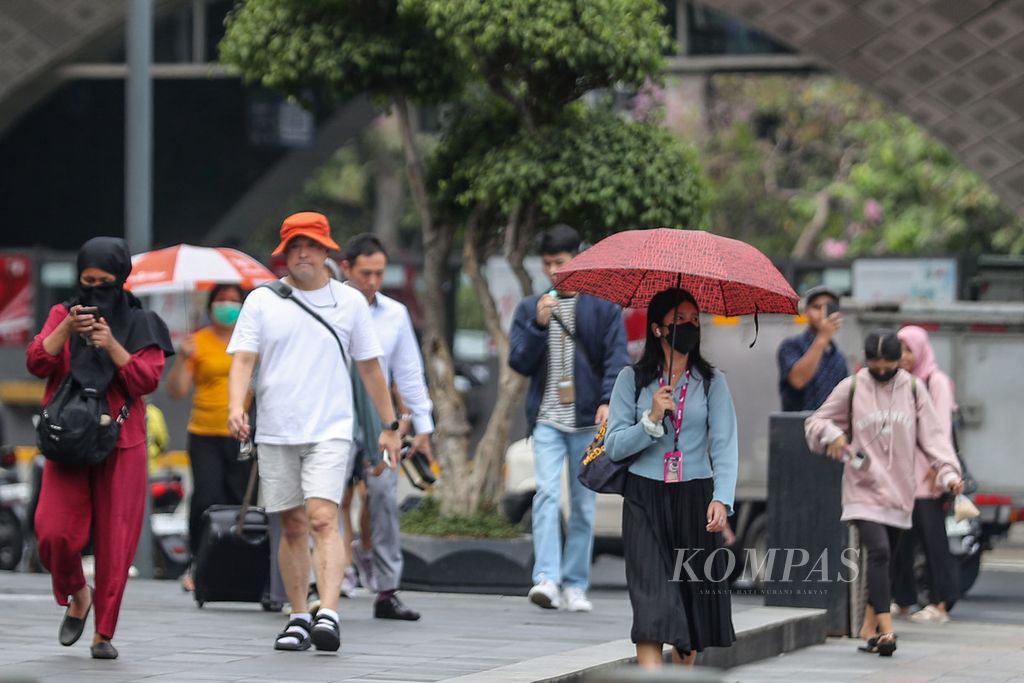 Warga menggunakan payung saat berjalan di kawasan Bundaran Hotel Indonesia, Jakarta, Senin (9/10/2023).  