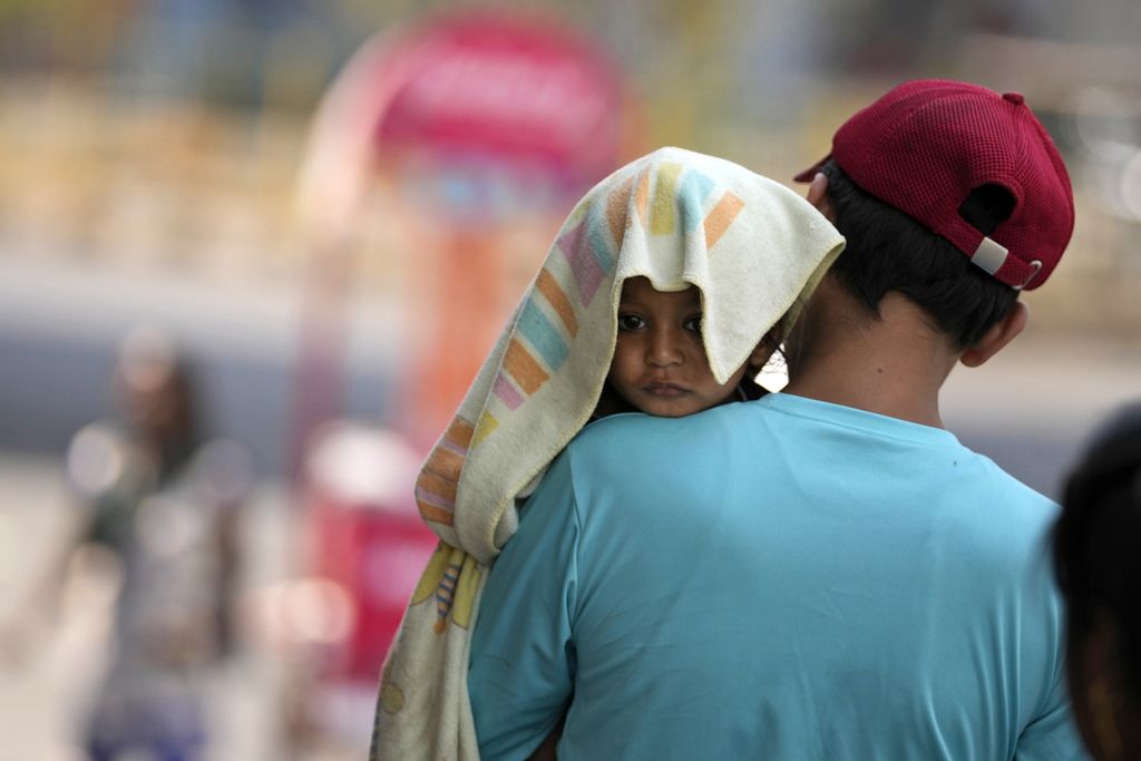 Kepala seorang anak ditutupi selembar handuk untuk mengurangi terik matahari yang menyengat kepala saat dia digendong oleh sang ayah di salah satu sudut kota Jammu, India, Minggu (2/6/2024). 