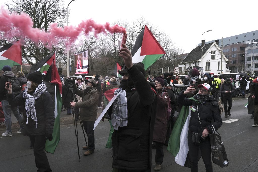 Para pengunjuk rasa mengibarkan bendera Palestina saat mereka berbaris di depan layar video raksasa yang memproyeksikan sidang langsung selama demonstrasi di luar Mahkamah Internasional di Den Haag, Belanda, Kamis (11/1/2024). 